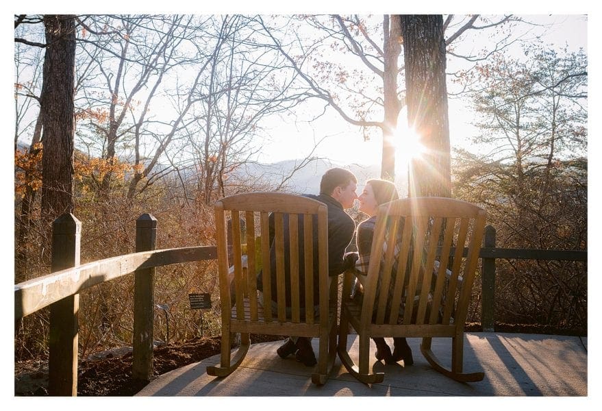 young engaged couple sitting on deck kissing at sunset
