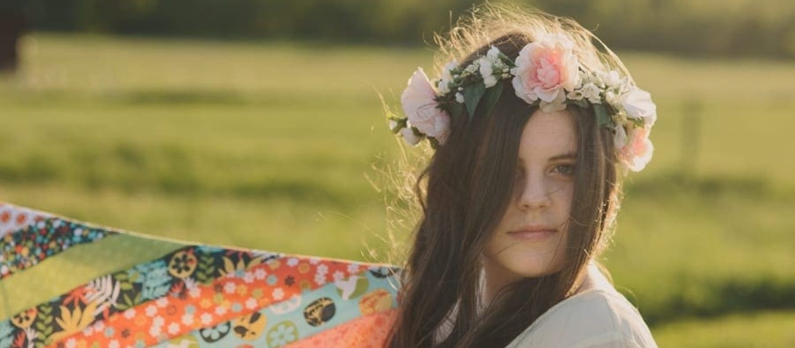 I headshot of a teen holding a fabric kite while standing in a field wearing a flower crown and rim lighting of her hair